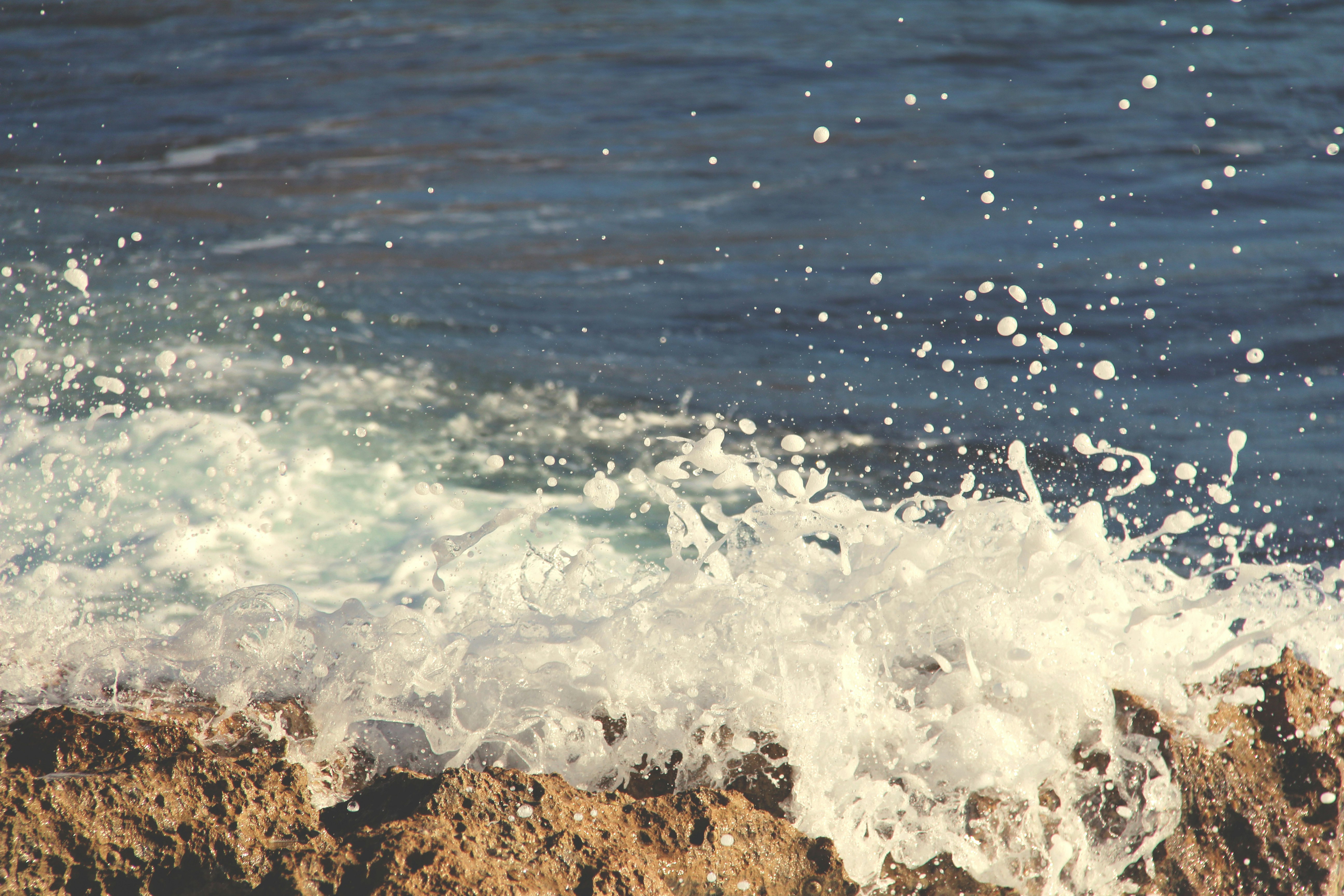 photo of sea wave bump into boulder